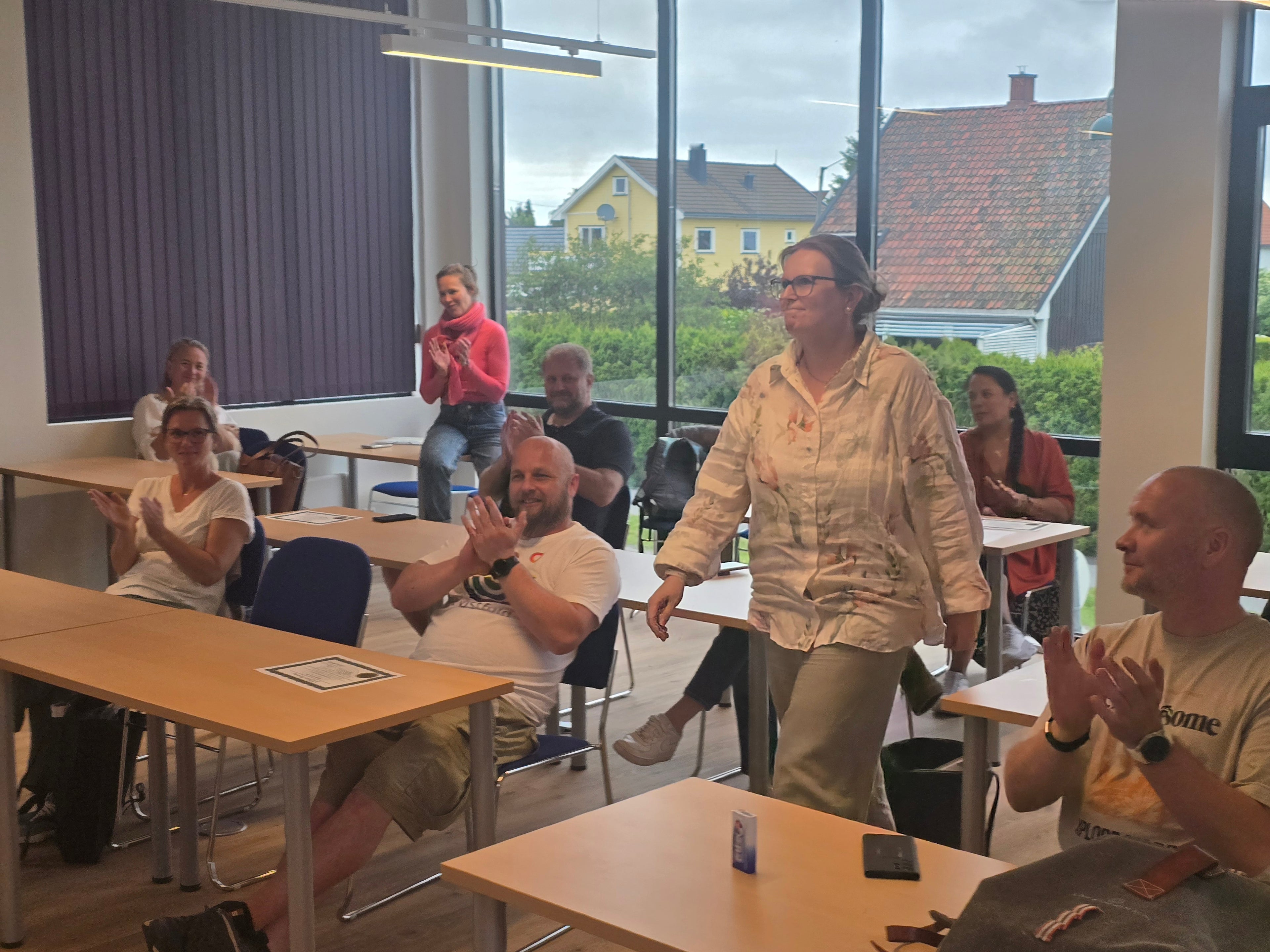 En deltaker går gjennom kursrommet mens gruppen applauderer under NLP Practitioner-utdanningen.